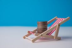 Happy stack coins rest on wooden beach chair with blue background in summer beach holiday. Financial freedom through passive income.