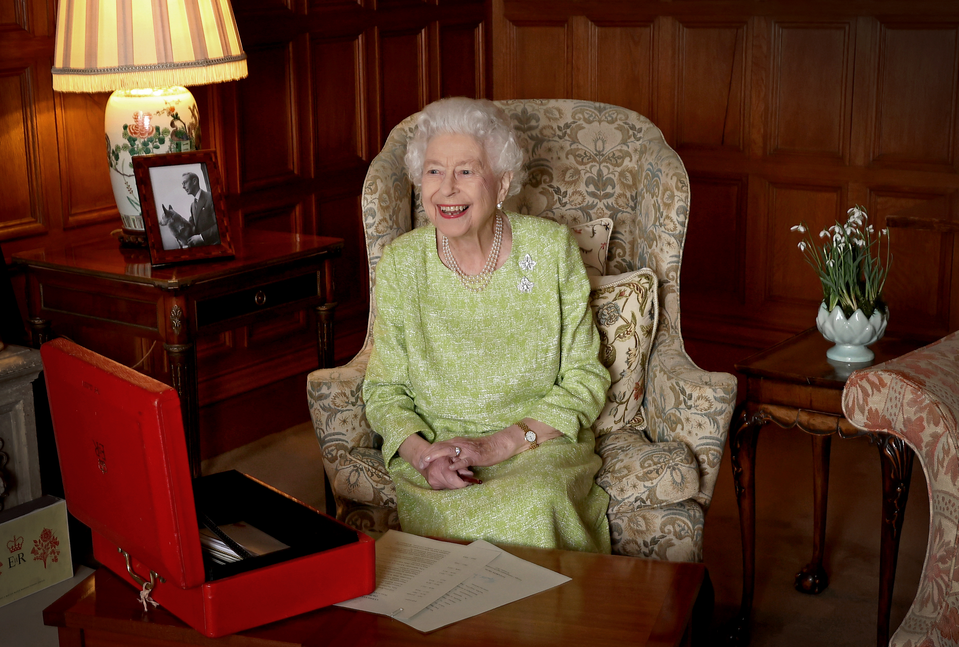 Queen Elizabeth wearing a green dress sitting at a desk with her red box