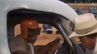 Richard Pryor with a helmet and googles, sitting in a race car.