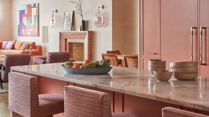 pink kitchen with bowls on marble countertop, pink kitchen cabinets, a pink fireplace, pink bar stools, and a blue platter filled with fruit and vegetables