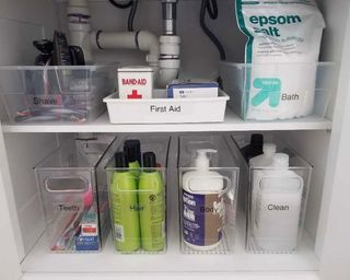 An under the sink bathroom vanity with bathroom products in acrylic bins