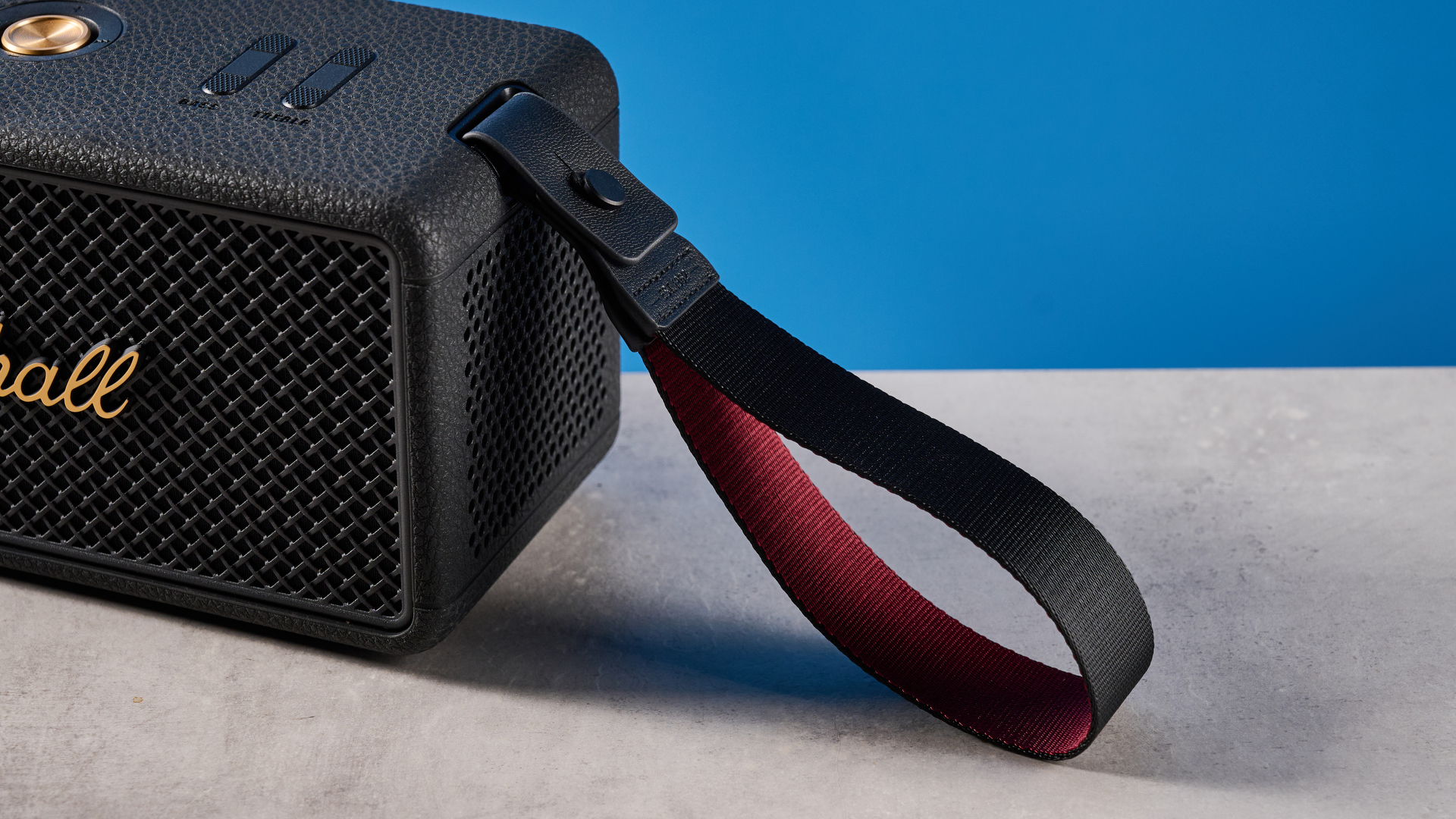 The Marshall Middleton II Bluetooth speaker in Black and Brass, on a stone surface with a blue wall in the background