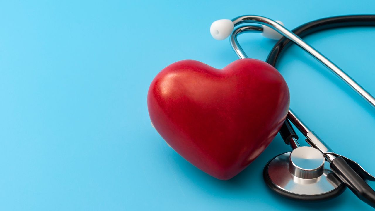 Red heart balloon next to stethoscope on blue background.