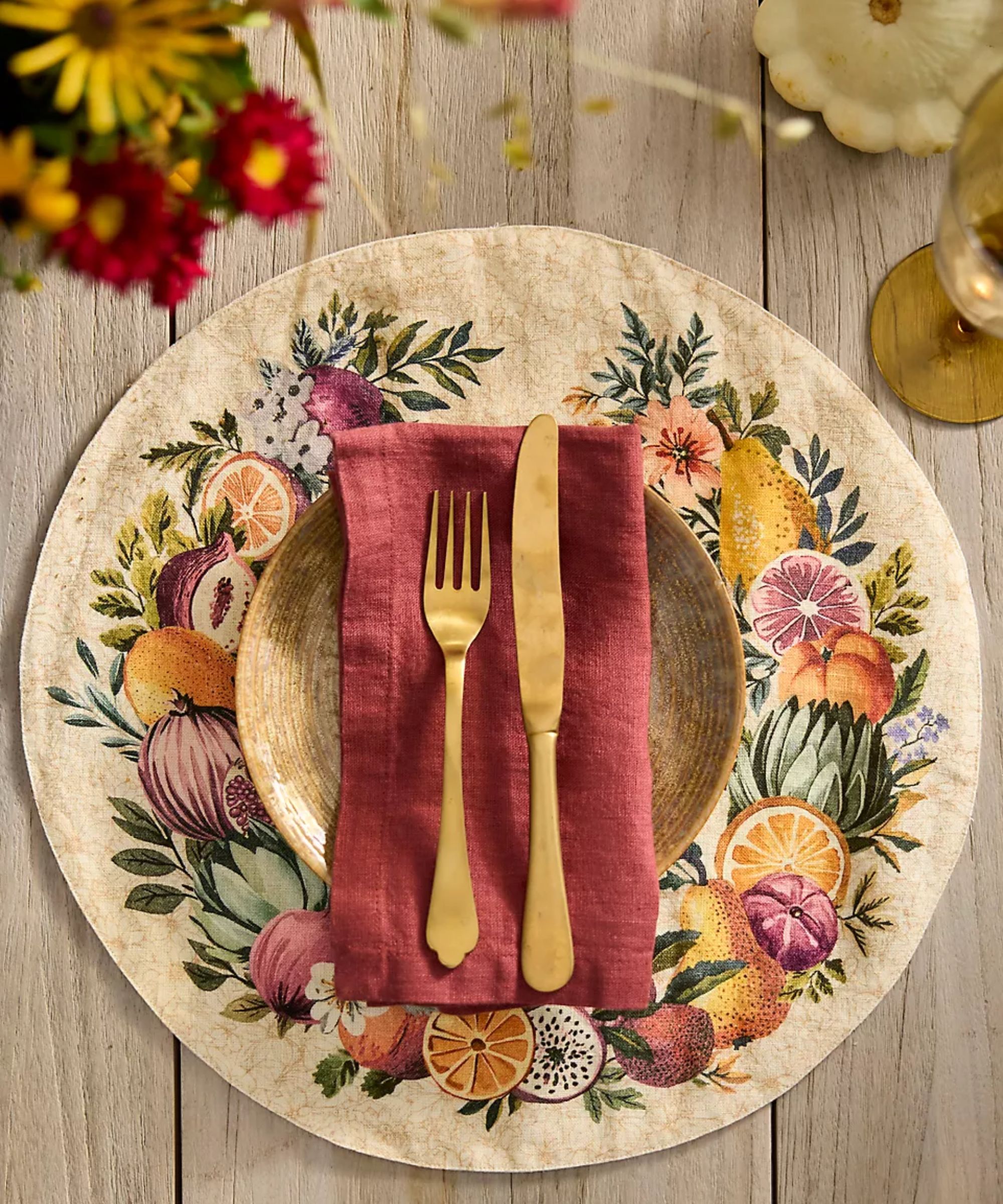 Red linen napkin and gold cutlery on top of a taupe linen placemat with harvest motifs