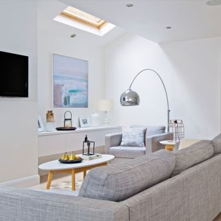 small white living room with grey corner sofa a wall TV and chrome floor lamp