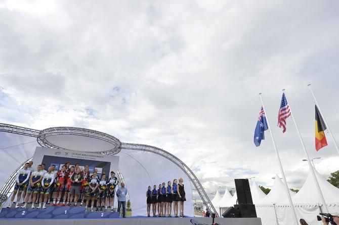 The teams on the podium reflect as the national flags are hoisted