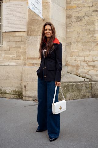 Katie Holmes wears a navy blue and red jacket, dark blue denim jeans, black shoes and a white bag outside Patou during the Haute Couture Fall/Winter 2024/2025 as part of Paris Fashion Week on June 27,