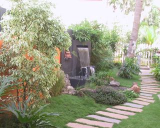 A tropica-themed backyard with garden path and water feature