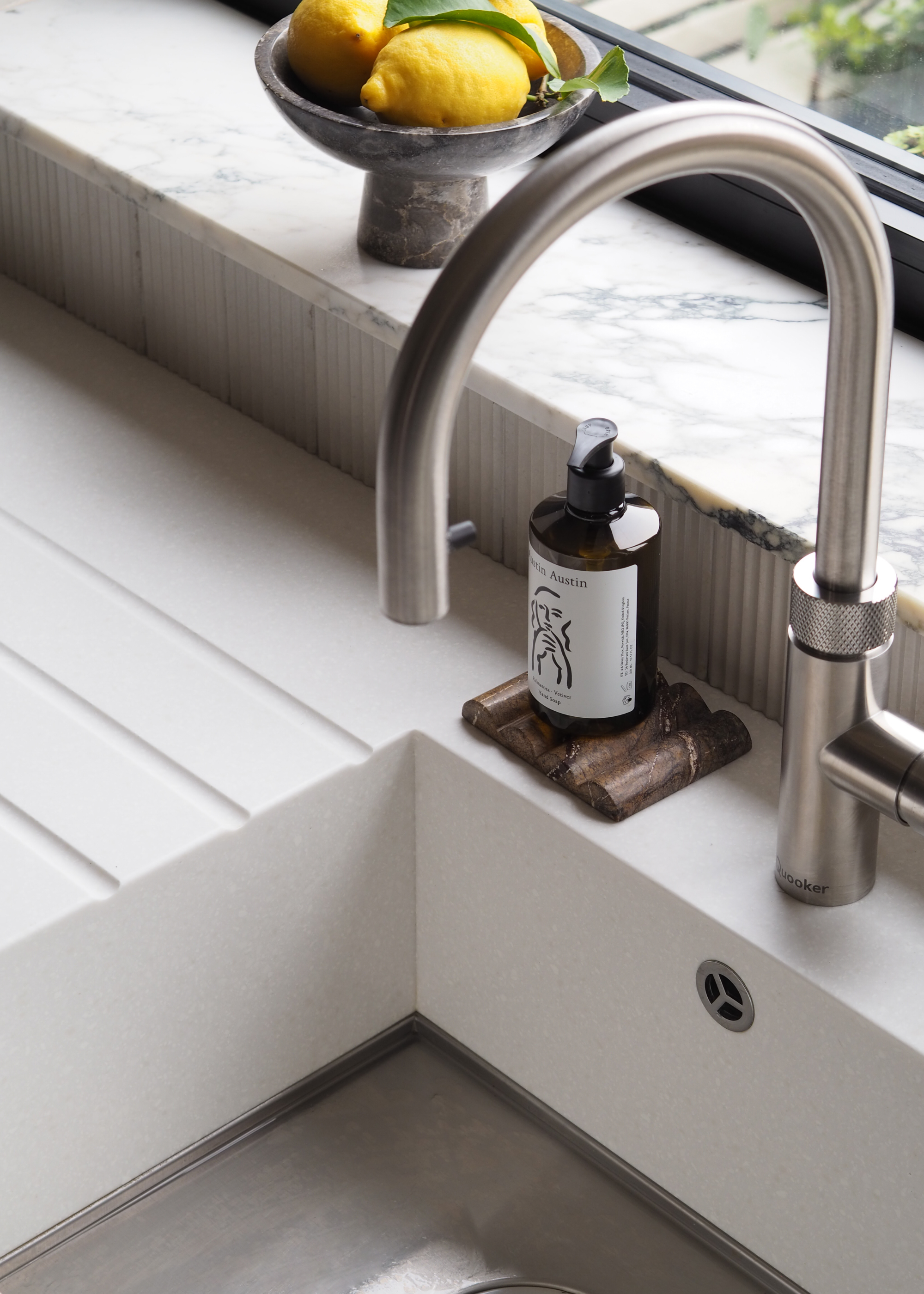 an inset kitchen sink with a tap as well as dish soap beside the table and a bowl of lemons by the windowsill