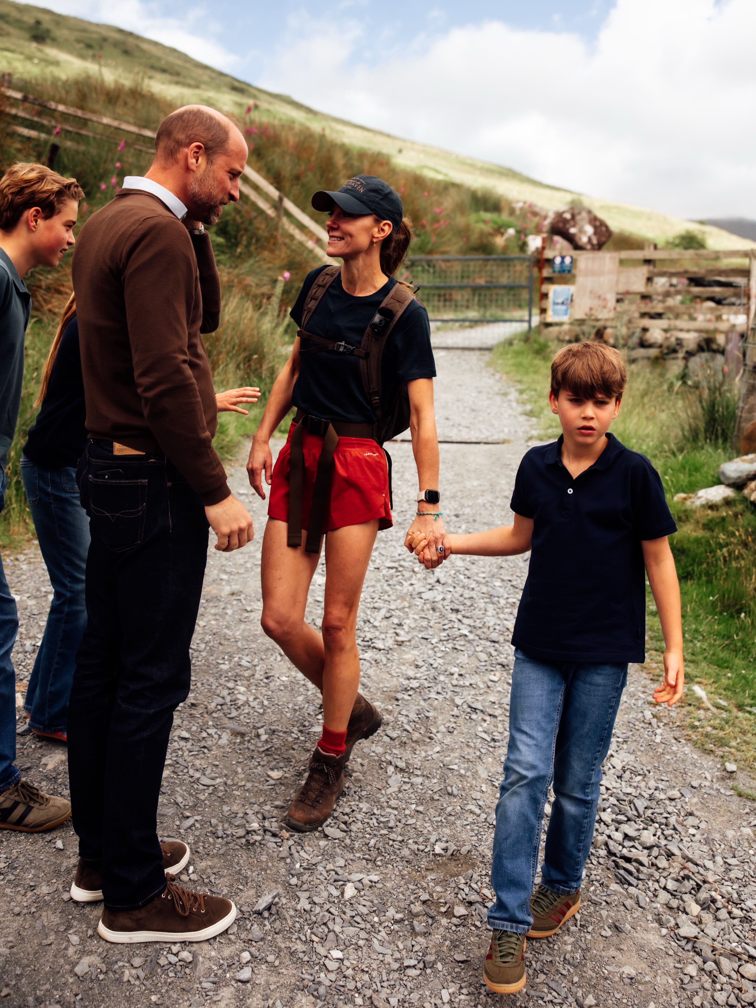 Princess Kate, wore is wearing red shorts and navy baseball cap, is greeted by her three children, Princess Charlotte, Prince George, and Prince Louis, who all wear matching denim jeans