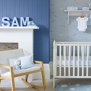 Blue nursery with white fireplace and cot, and armchair with blue cushions