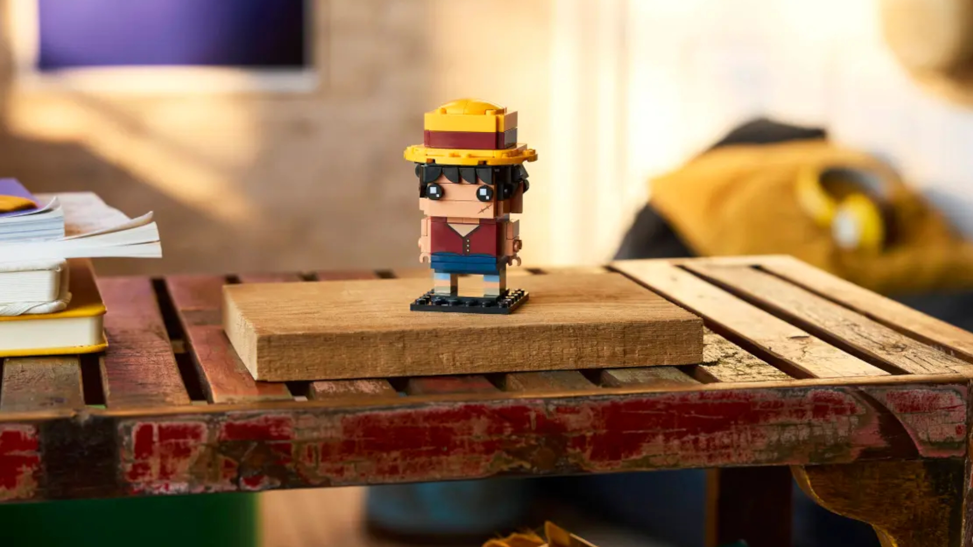 The Monkey D. Luffy BrickHeadz figure standing on a flat wooden block that is lying on an antique wooden table