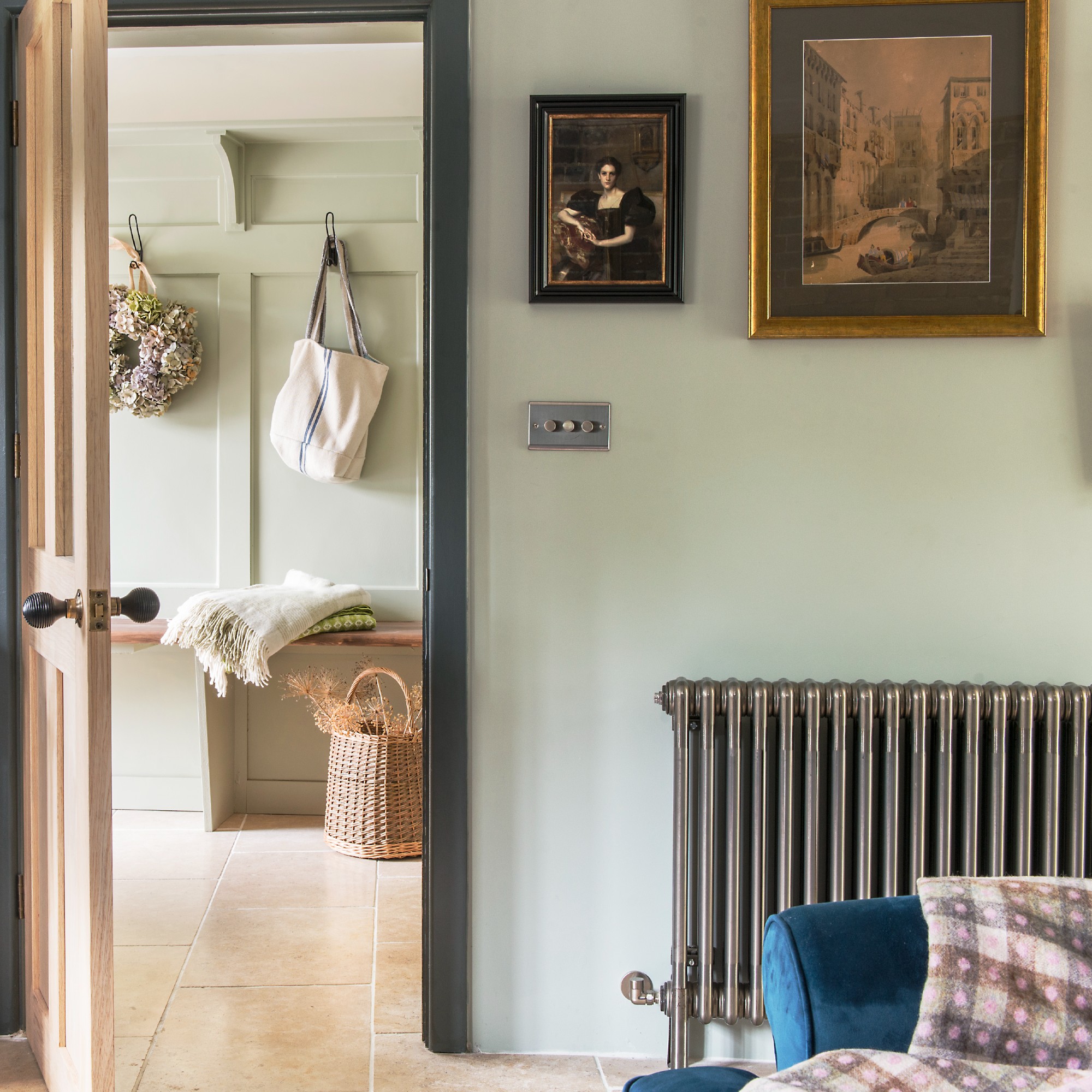 Traditional radiator on wall of pale green living room next to a doorway that leads to a hall with a bench and basket