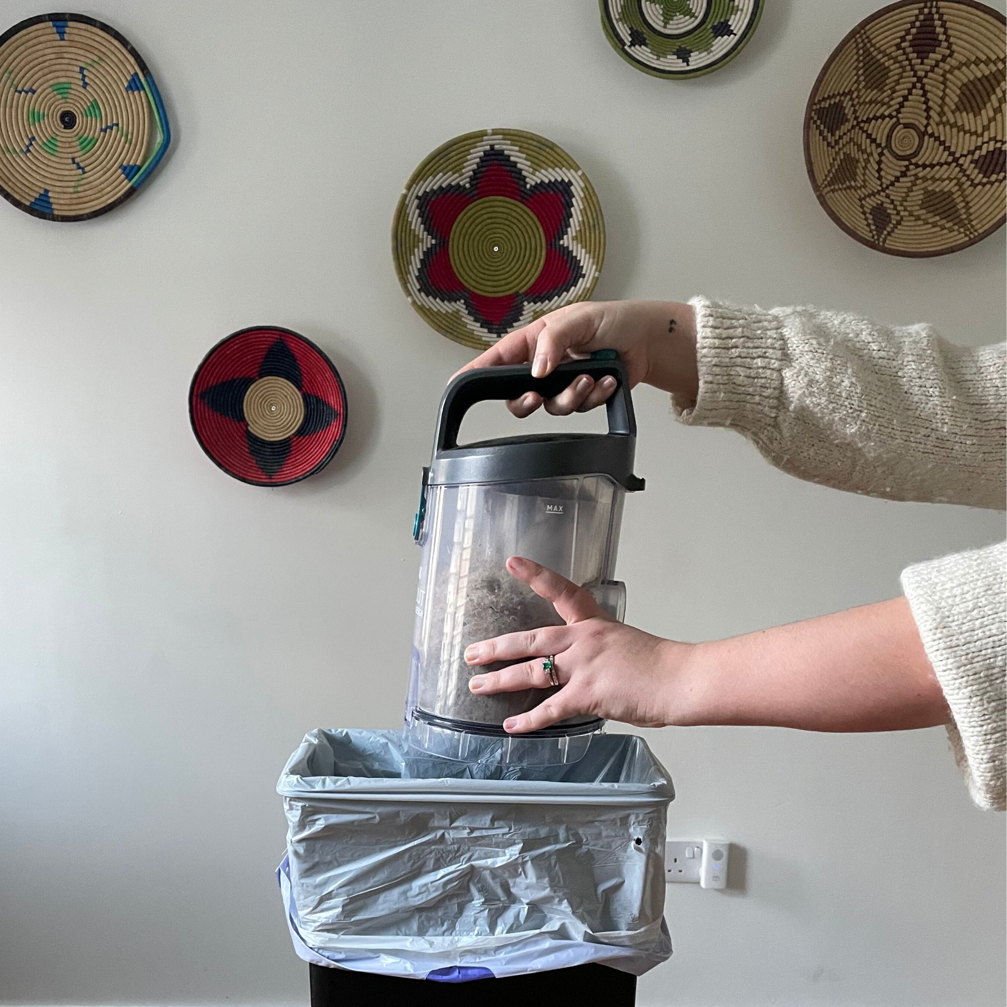 Emptying the Vax LiftOut Reach Pet Design Vacuum Cleaner in front of a white wall with colourful baskets on it