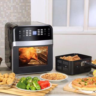 Black air fryer oven cooking food on kitchen worktop surrounded by plates of food