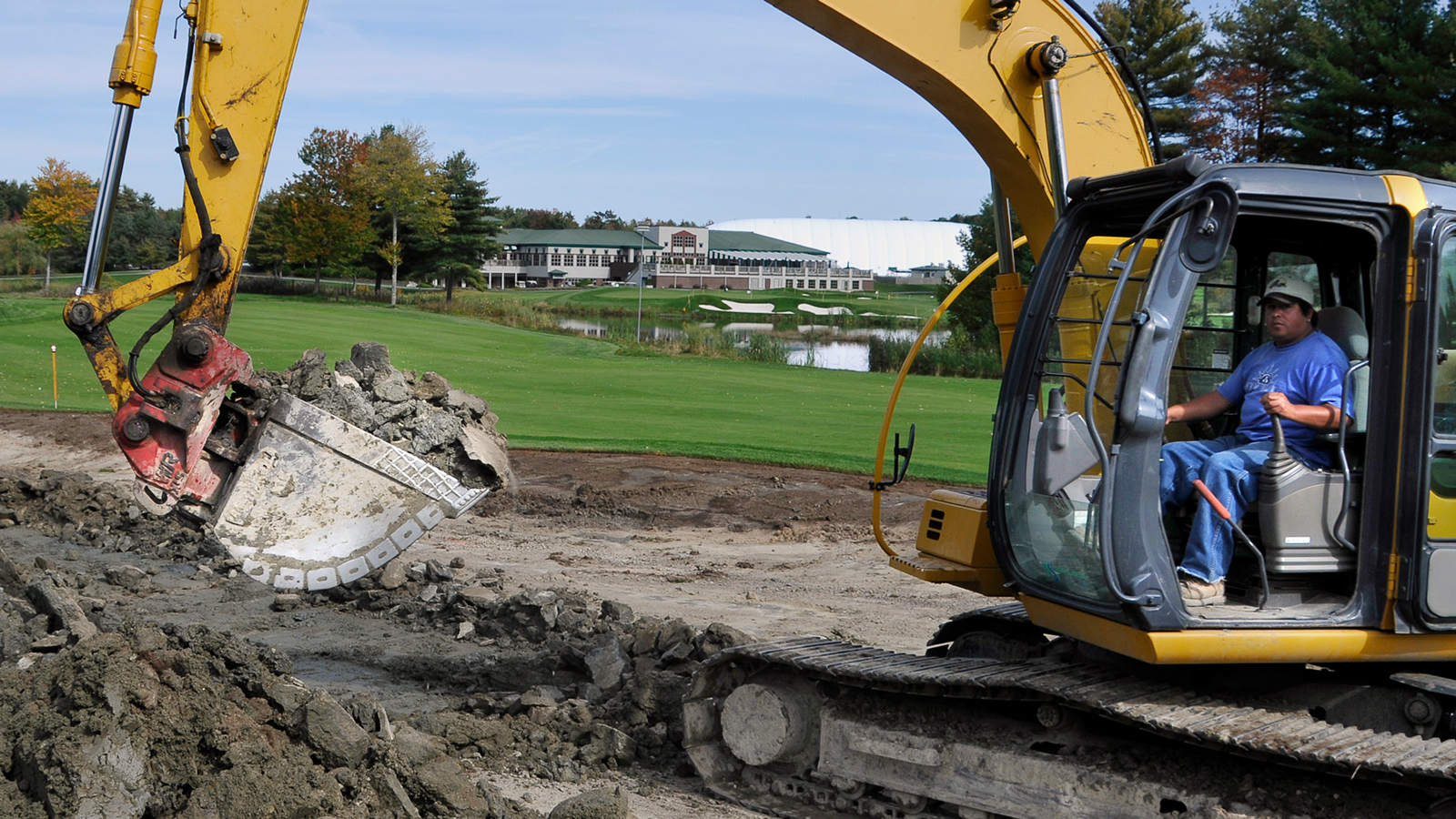 A digger digs up turf next to a golf course