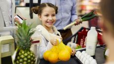 A young girl holds a bag of lemons at the checkout counter of a supermarket.