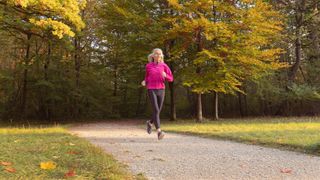 Woman running along path in fall smiling and wearing running clothes