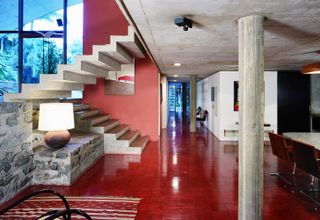 Interior of concrete house with open staircase, red floor and pillars