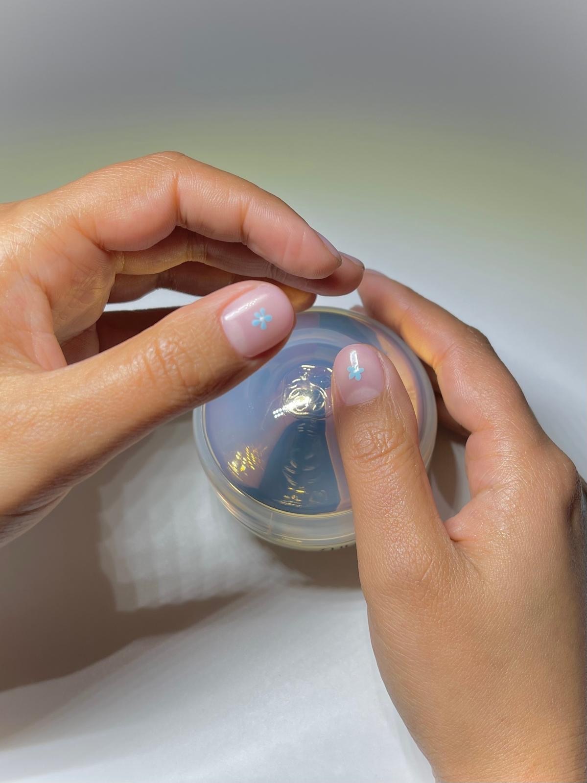 Harriet Westmorelands hands, showcasing her blue floral nail art while holding a blue moisturiser