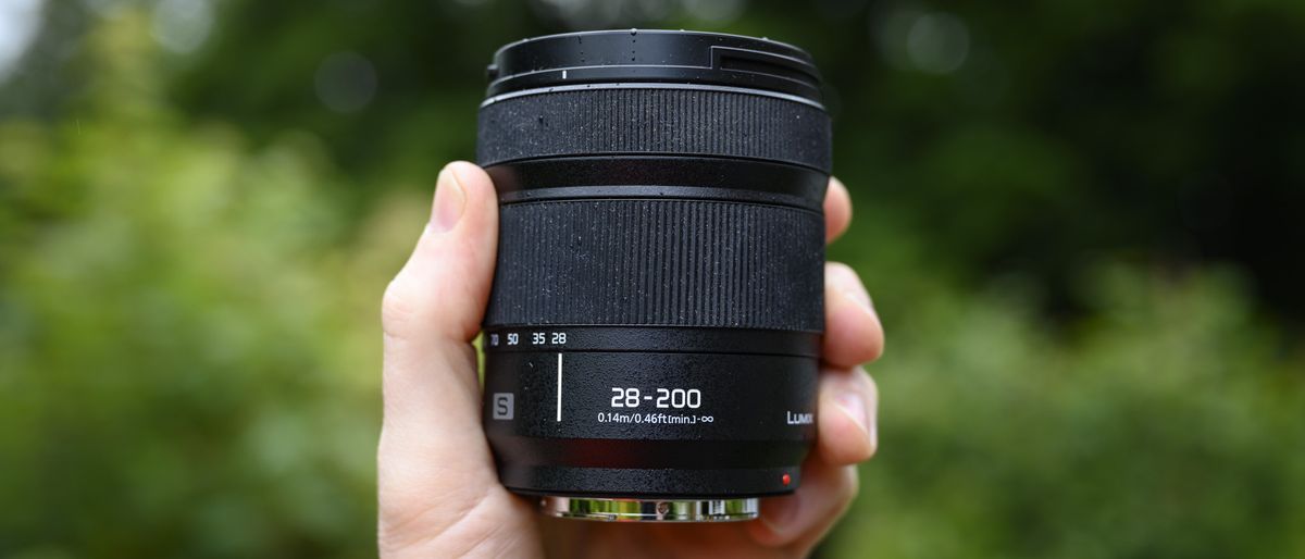 Panasonic Lumix S 28-200mm travel lens in the hand with leafy background and light rain