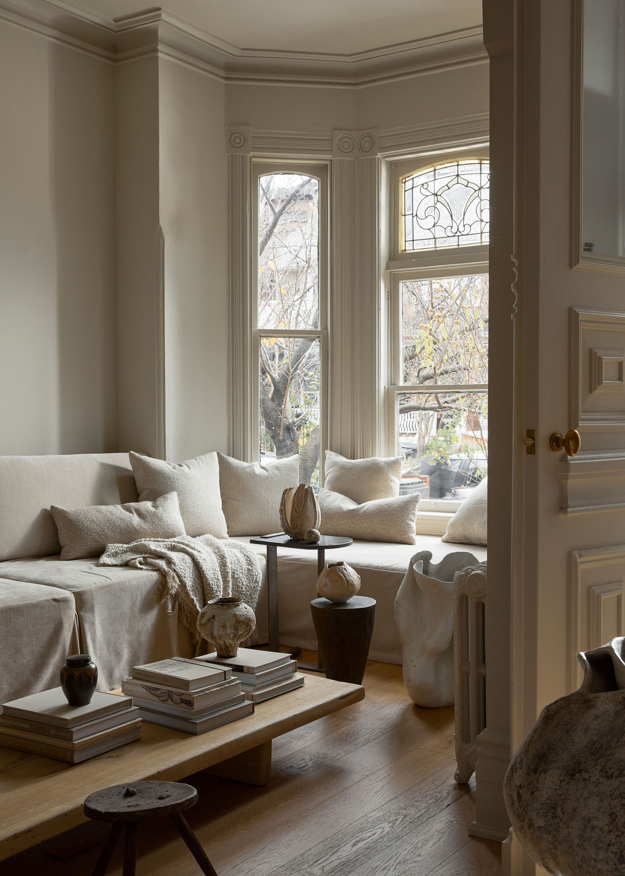 A cozy white living room with layered throws, pillows, and stacks of books with vases