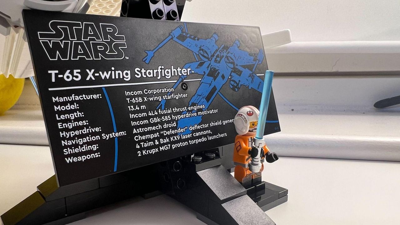 Lego Star Wars X-Wing Starfighter 75355-plaque front view with Rebel Pilot Luke minifigure standing in front holding blue lightsaber.