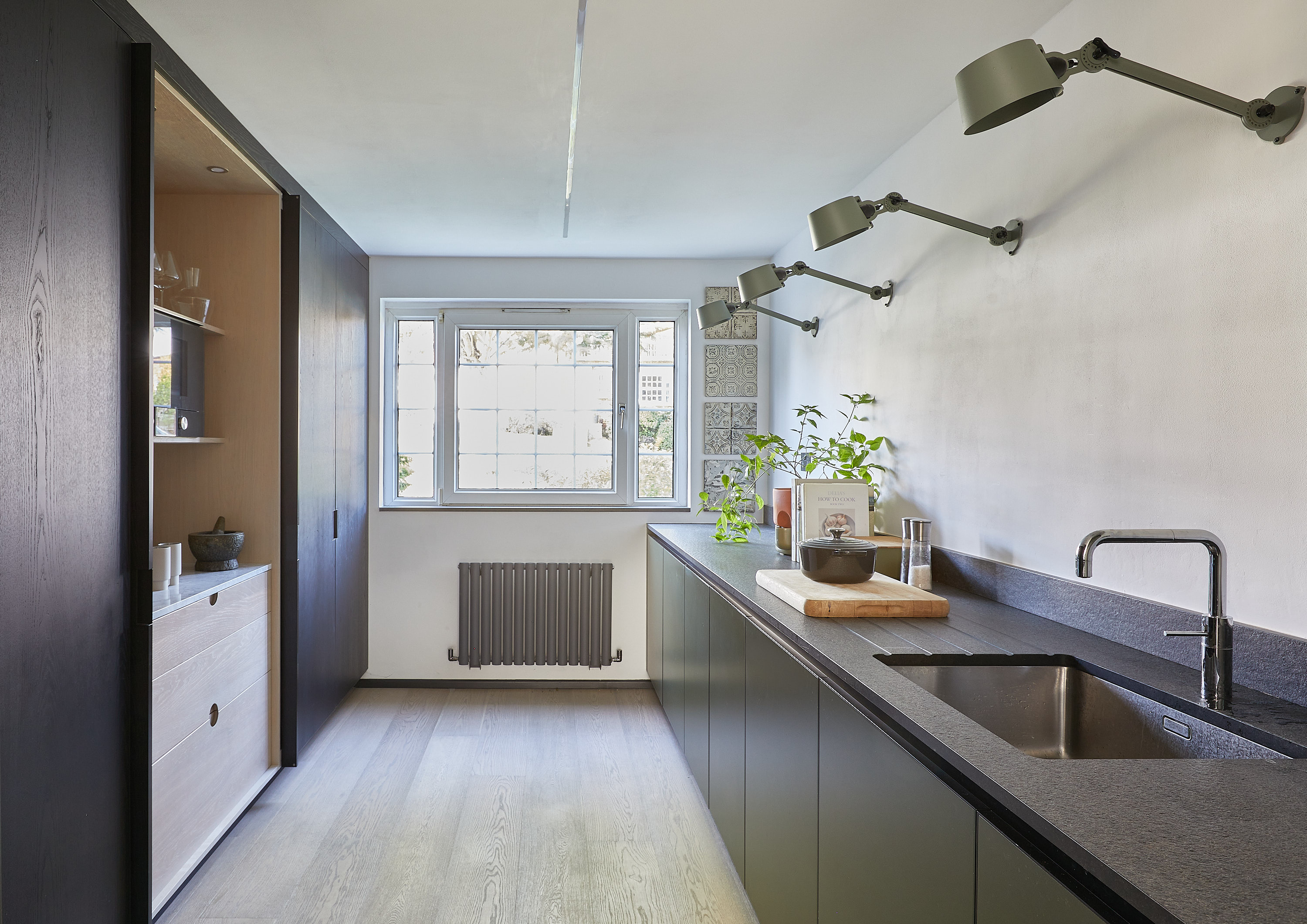 A galley kitchen with full height cabinets along one side and base unit along the other and some statement wall lights above