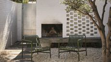 an exterior firepit in a brick wall with a gtavel garden and modern green chairs