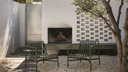 an exterior firepit in a brick wall with a gtavel garden and modern green chairs