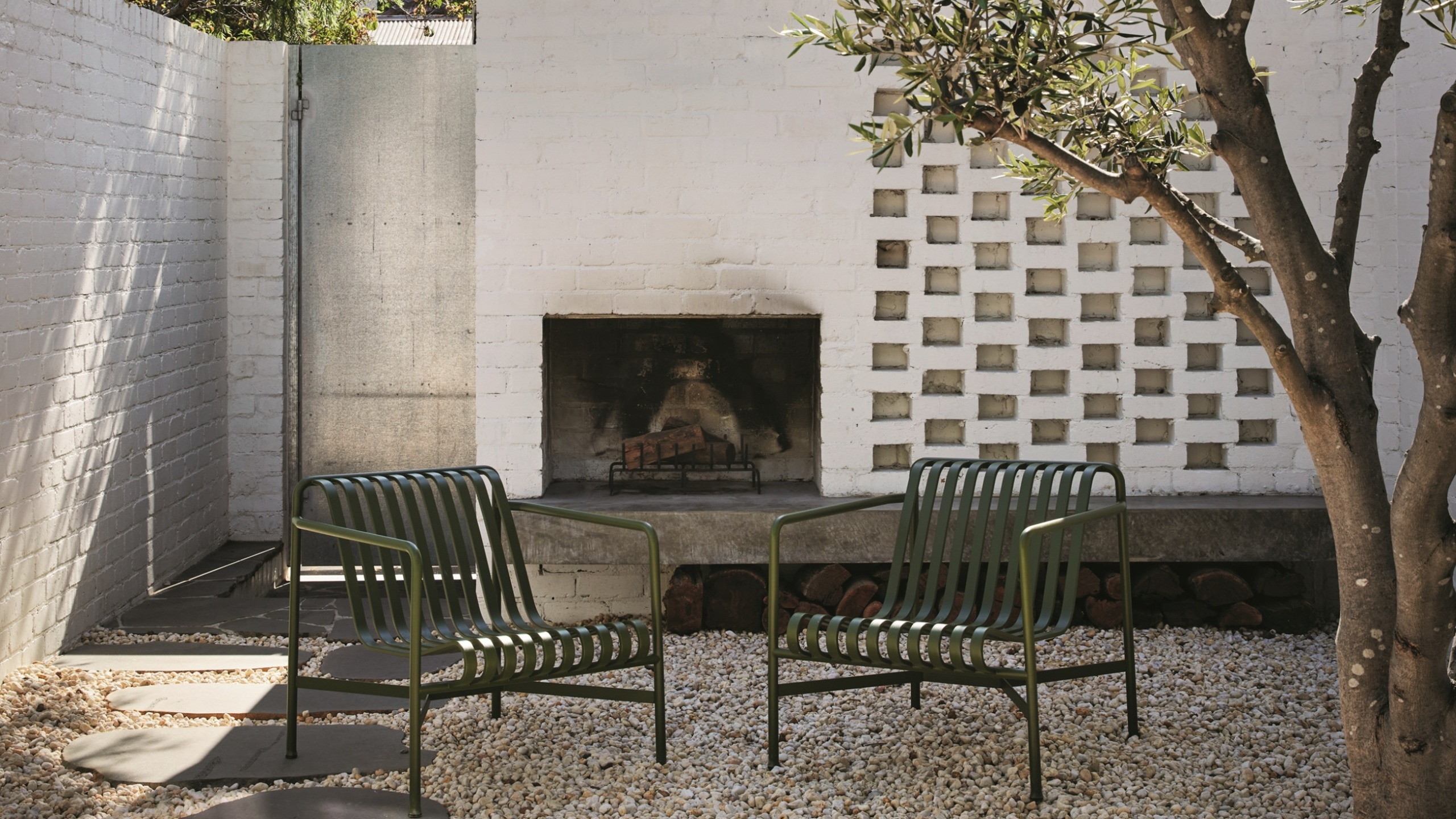 an exterior firepit in a brick wall with a gtavel garden and modern green chairs
