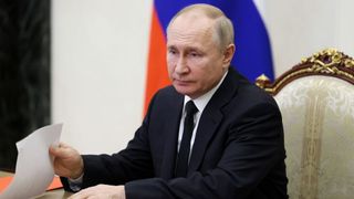 Vladimir Putin shuffling papers at a desk.