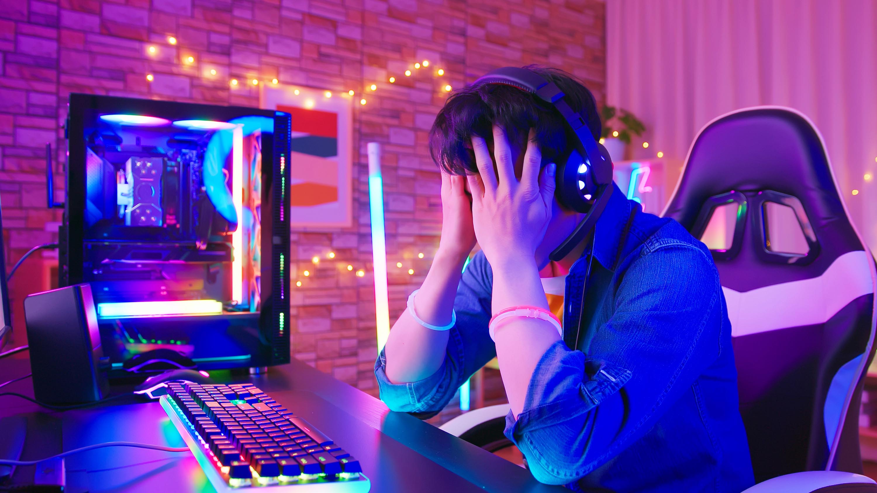 Asian male esport gamer plays exciting online game in room with neon lighting - he lost and feels upset