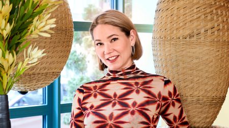 Designer Minnie Kemps stands in front of rattan funirture wearing a red, cream, and black top.