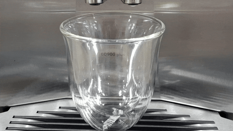 Coffee maker dispensing steamed milk into glass cup
