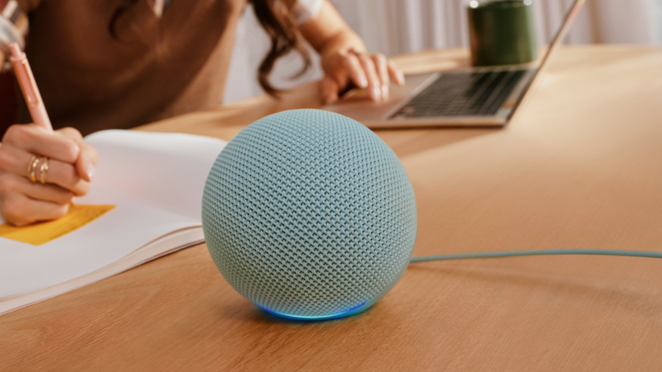 Echo Dot (6th gen) smart speaker on a desk in front of a lady working