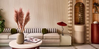 A cream-colored hotel lobby is filled with stripy, checkered, and terrazzo surfaces and furniture in organic tones of bordeaux, green, and ochre.