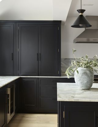 Black kitchen cabinets with marble worktops, white walls and pale wooden flooring.