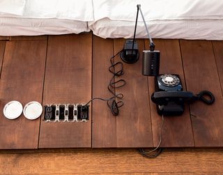 A detail of a sleeping platform with electrical outlets, a black lamp, and a black rotary phone.