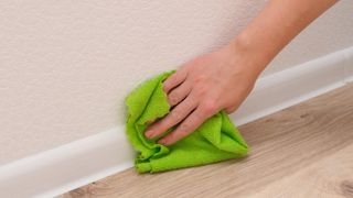 A woman's hand cleaning a skirting board with a green microfibre cloth