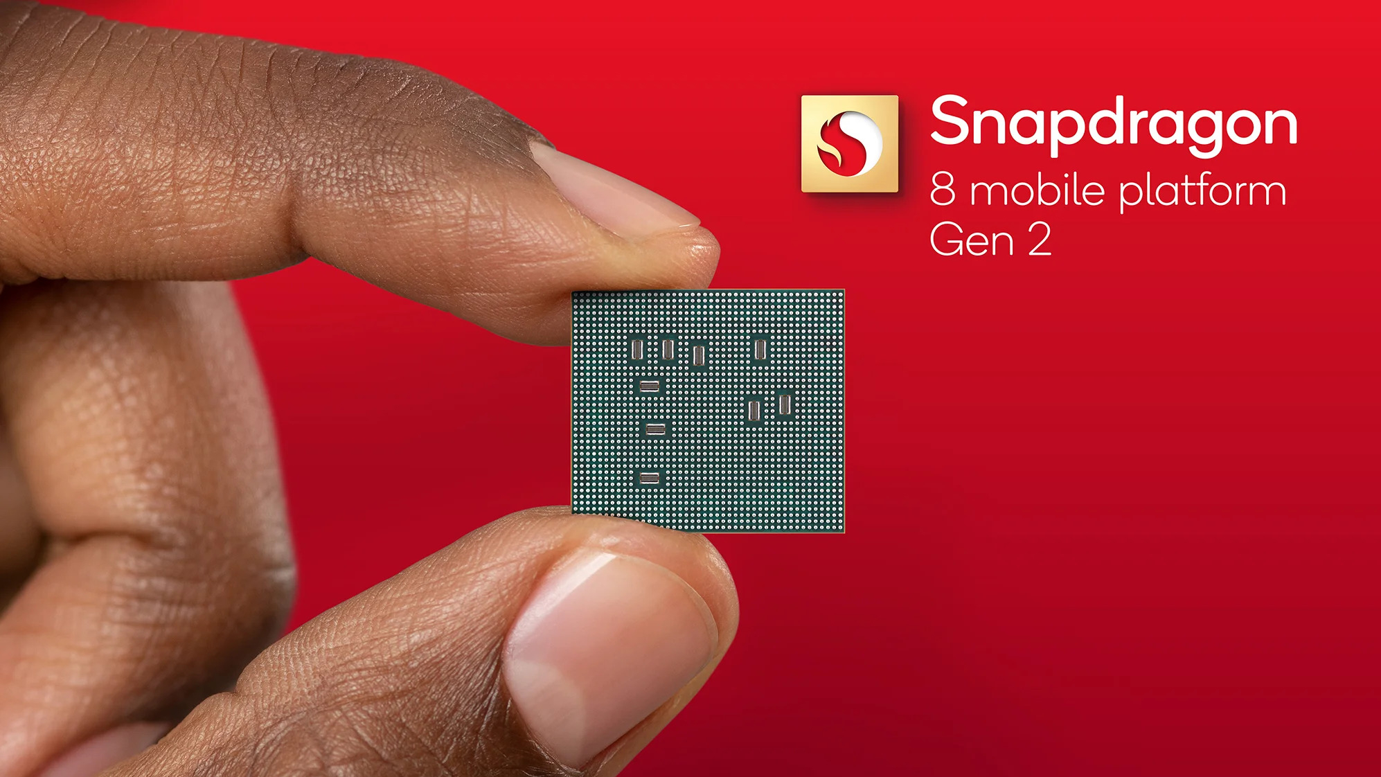 Image of fingers holding Qualcomm Snapdragon 8 Gen 2 chip on a red background