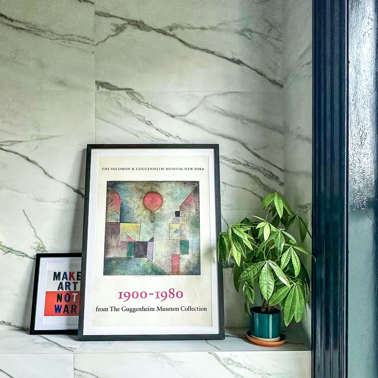 Pot plant and two framed artworks on ledge in marble bathroom