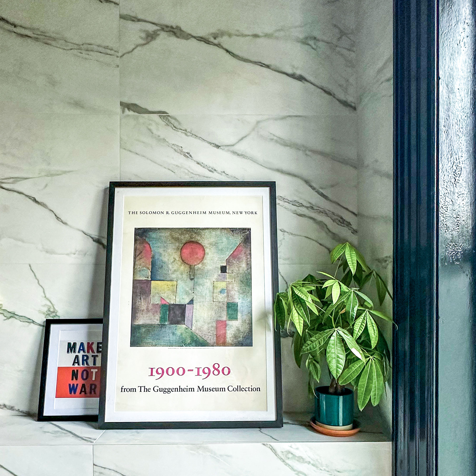 Pot plant and two framed artworks on ledge in marble bathroom