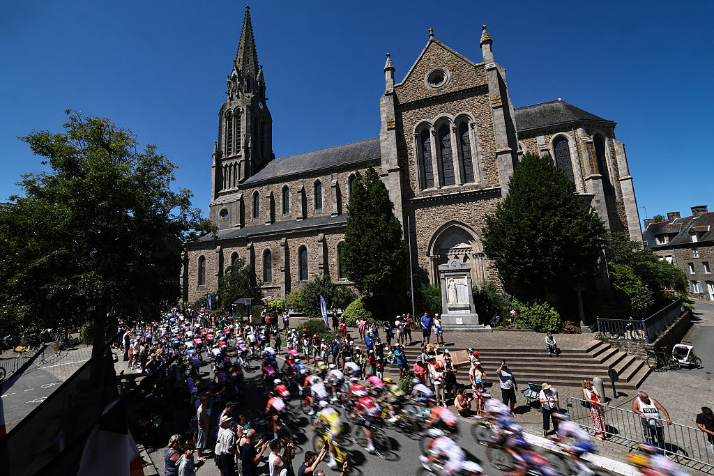 The pack of riders (peloton) cycles past the Notre-Dame church in Pleudihen-sur-Rance during the 7th stage of the 112th edition of the Tour de France cycling race, 197 km between Saint-Malo and Mur-de-Bretagne Guerledan, in Brittany, western France, on July 11, 2025. (Photo by Anne-Christine POUJOULAT / AFP)