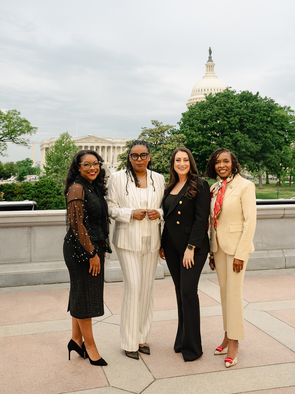 Four congresswomen pose together on the Capitol grounds with the dome behind them. From left: Emilia Sykes, LaMonica McIver, Sara Jacobs, and Yvette Clarke.