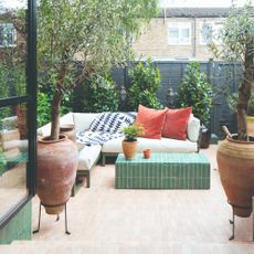 A tiled garden with a corner outdoor sofa with a green frame and cream cushions and tonal green tiled coffee table