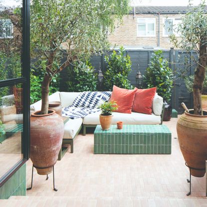 A tiled garden with a corner outdoor sofa with a green frame and cream cushions and tonal green tiled coffee table