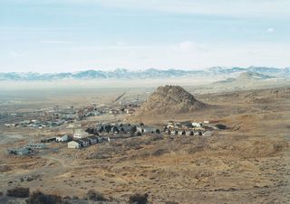 A birds-eye view of a village surrounded by country-side and mountain peaks in the distance.