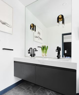 A white bathroom with a dark gray vanity and an oversized vanity mirror with two sconces installed onto the mirror