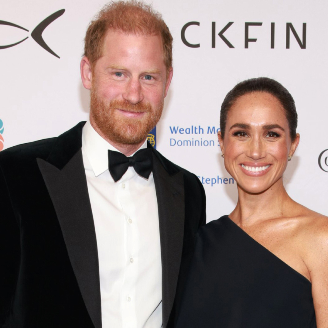 Prince Harry in a tux and Meghan Markle wearing a black gown on a red carpet